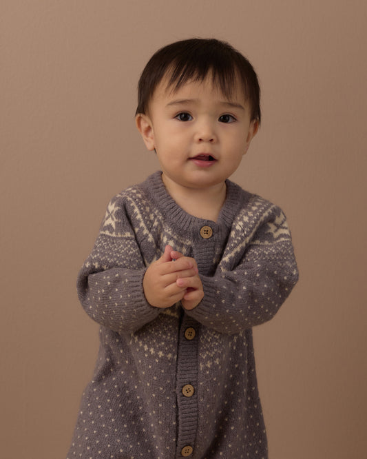 Baby wearing a grey fair isle knit romper with buttons down the front, in front of a beige background