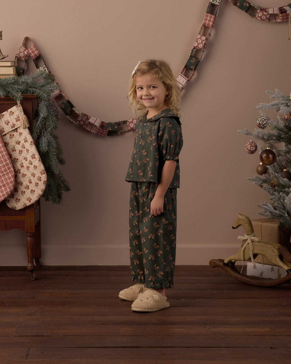 Child wearing green floral two piece pajamas in a living room decorated for Christmas