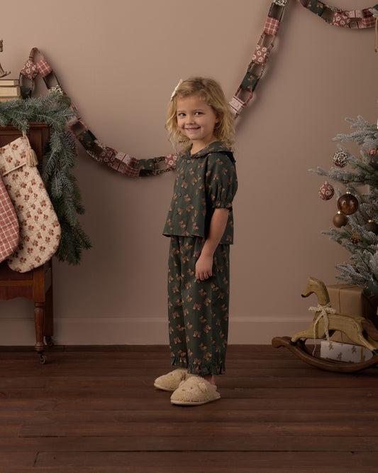 Child wearing green floral two piece pajamas in a living room decorated for Christmas