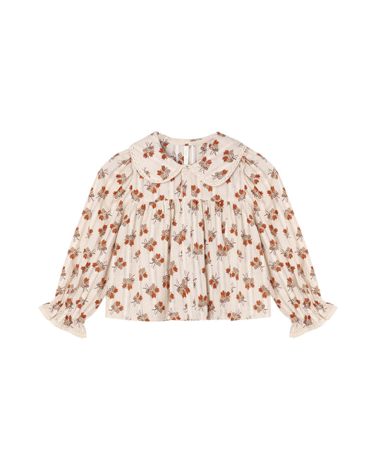 A long-sleeve blouse with a ruffled Peter Pan collar and ruffled cuffs, featuring an all-over floral print in orange, brown, and muted green on a warm cream background.