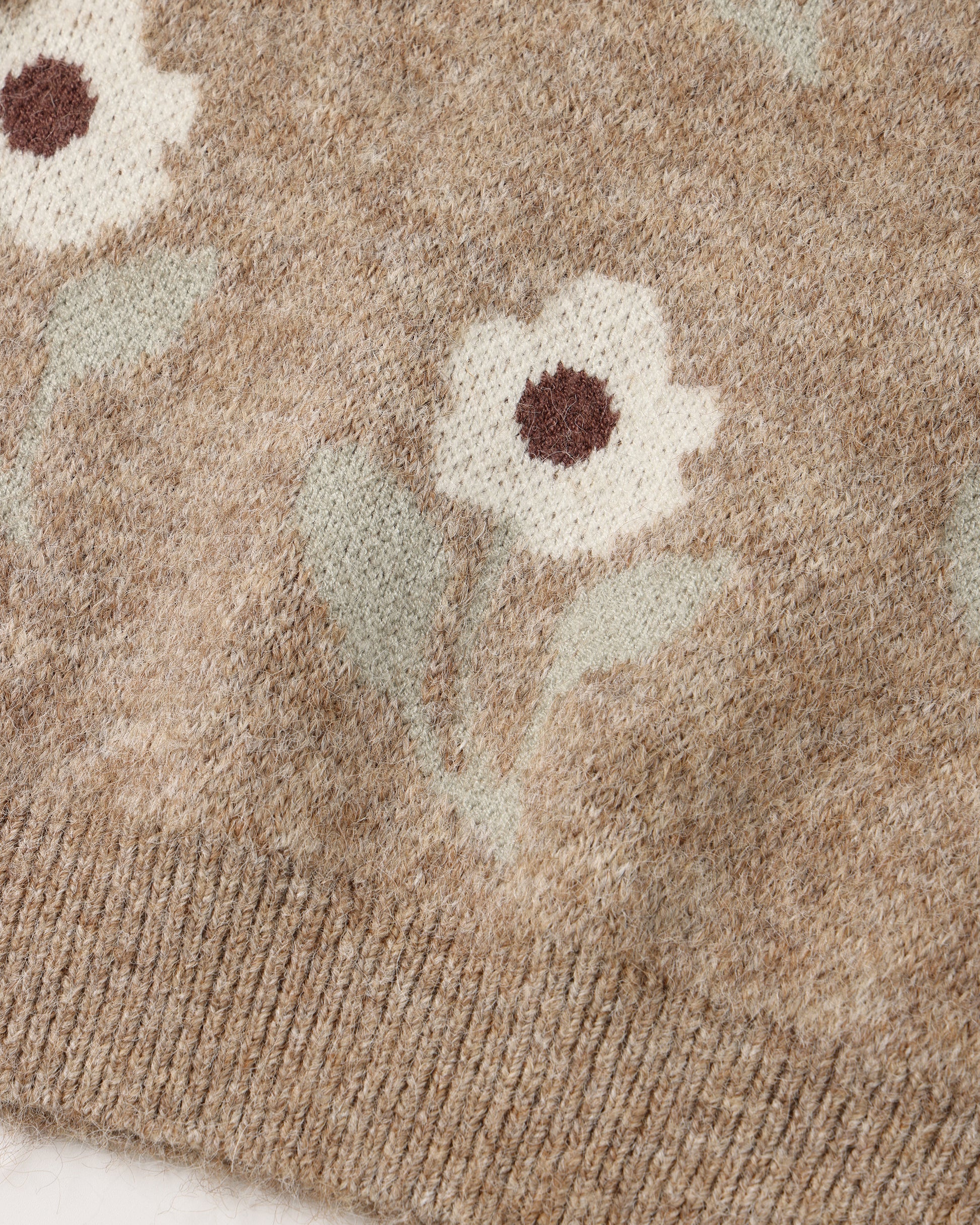 Close-up of a knit sweater showing a floral pattern in cream, sage green, and brown on a heathered taupe-beige background.
