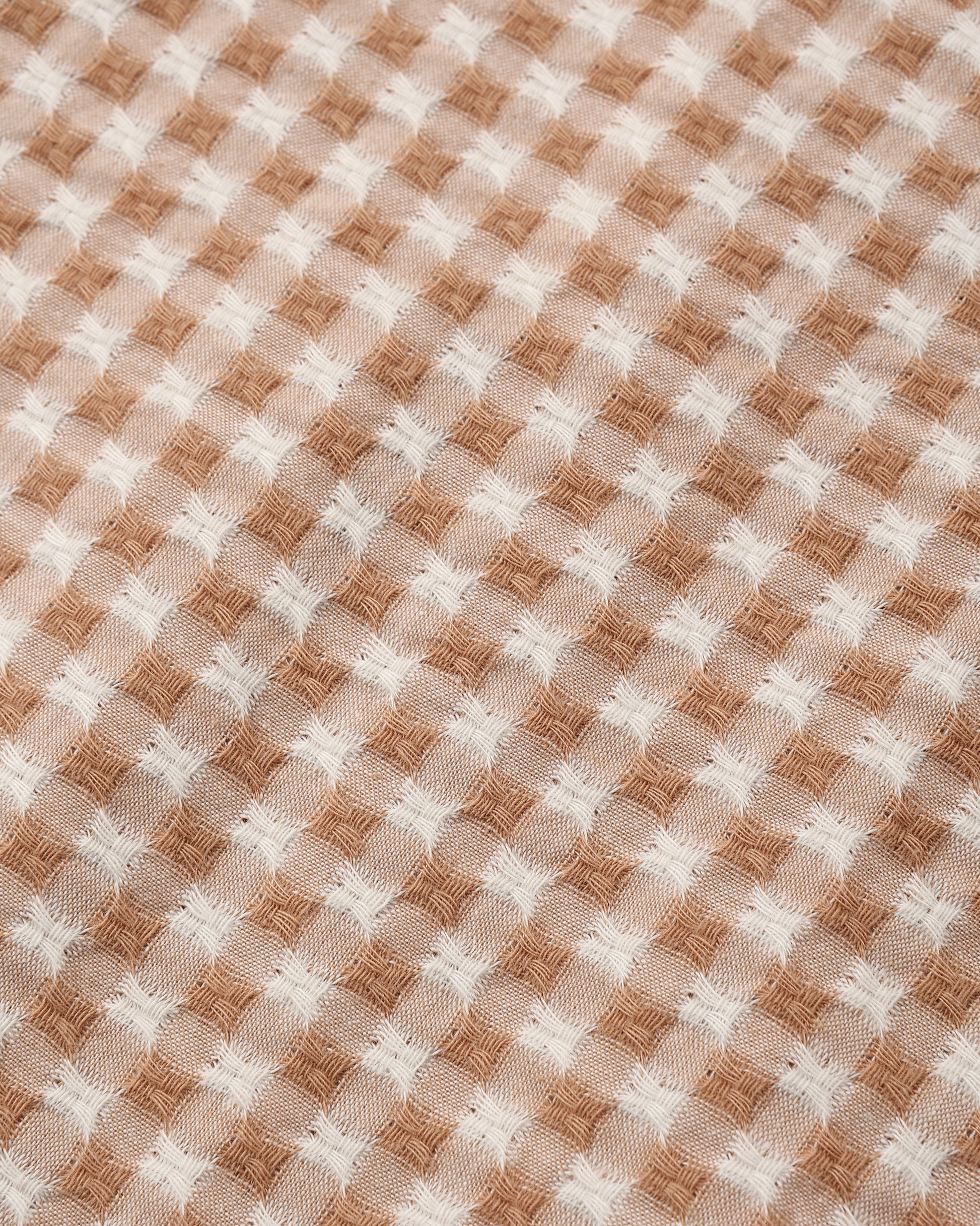 A close-up of a woven fabric with a tan and off-white gingham pattern.