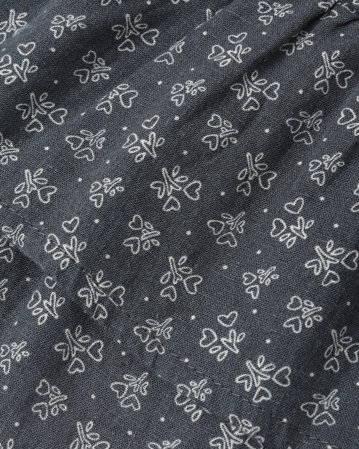A close-up of dark gray fabric with a repeating white embroidered pattern of small flowers, hearts, and dots.