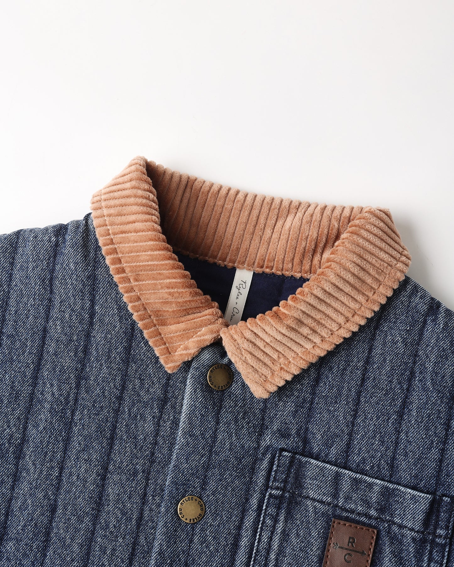 Close-up of a textured blue corduroy jacket with a tan corduroy collar and brass buttons, shown against a plain white background.