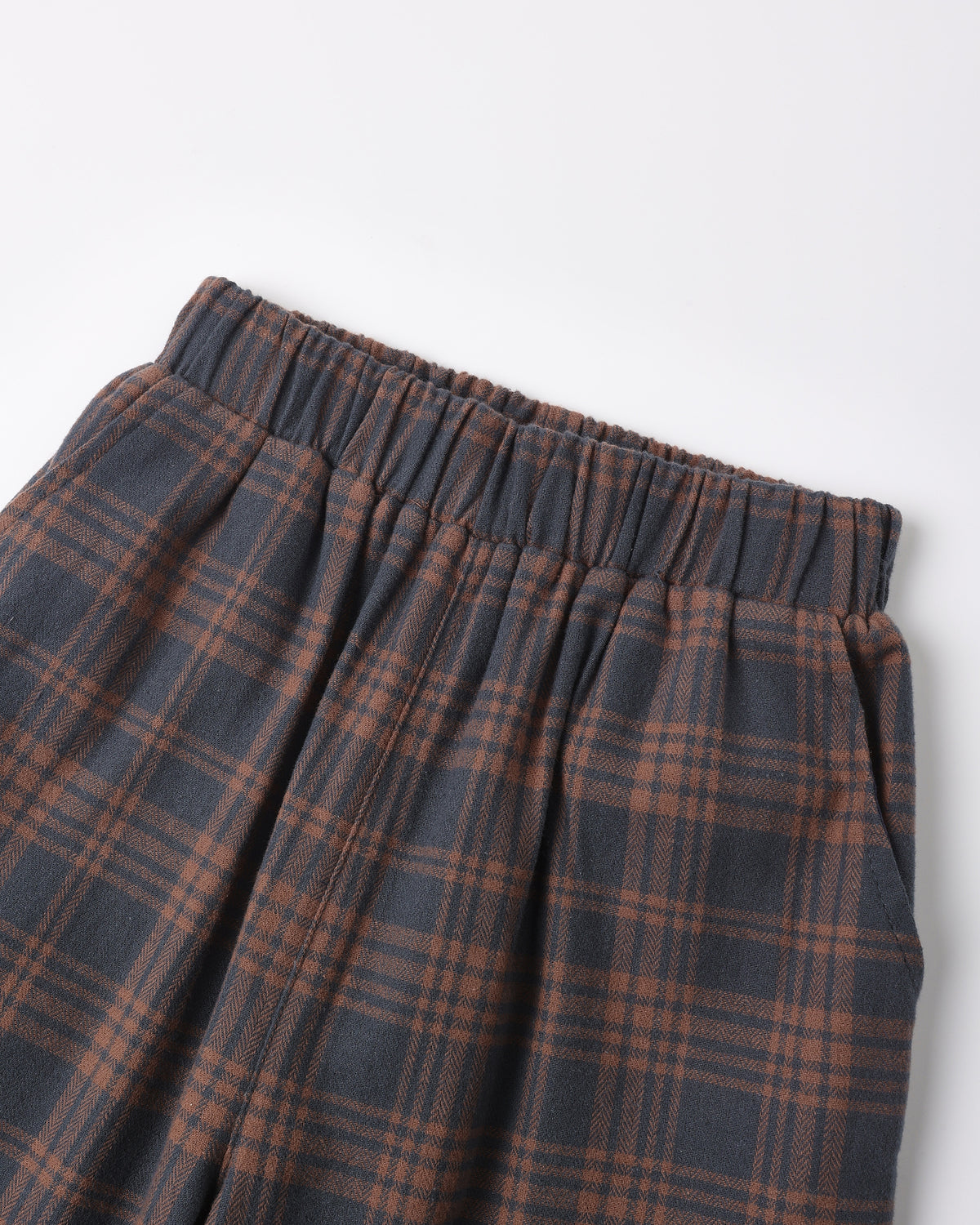 Close-up of a plaid skirt with an elastic waistband, featuring a dark gray and rust brown tartan pattern, shot against a plain white background.
