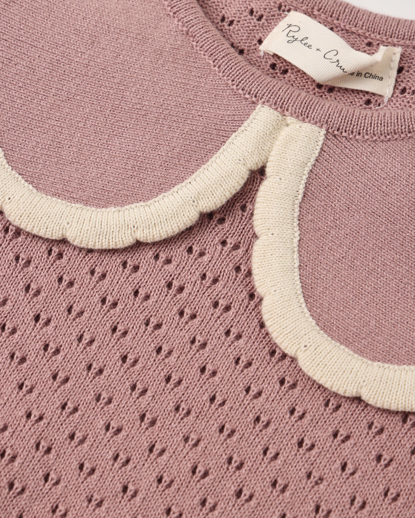 Close-up of a dusty pink knit sweater with a scalloped cream collar.