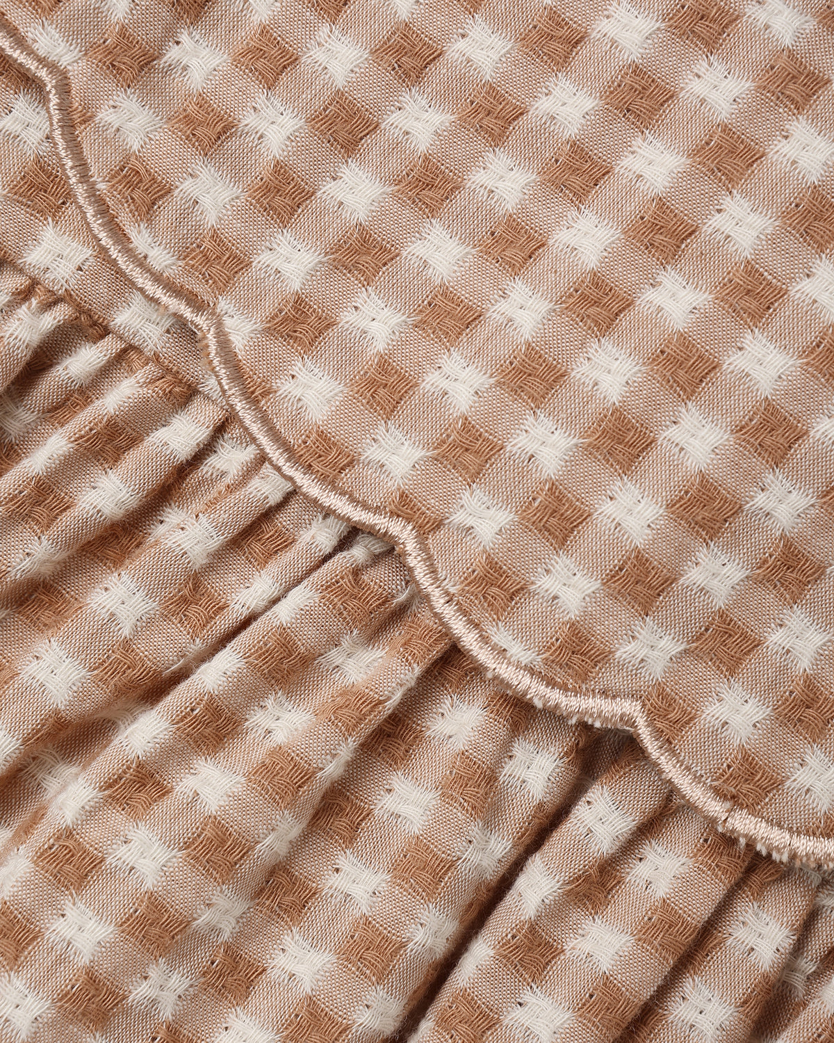 Close-up of a gingham fabric with a brown and white checkered pattern and a scalloped ruffle trim.