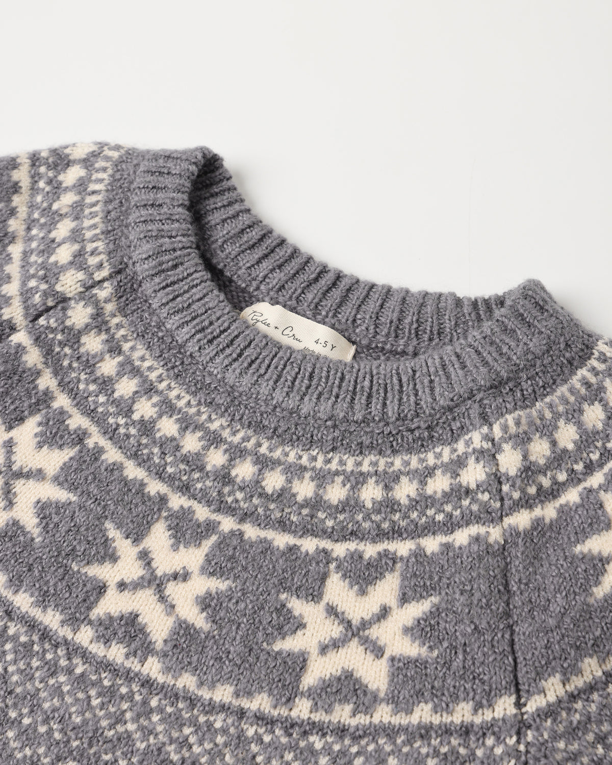Close-up of a gray knit sweater with cream-colored Fair Isle snowflake and geometric patterns, featuring a ribbed crew neck.