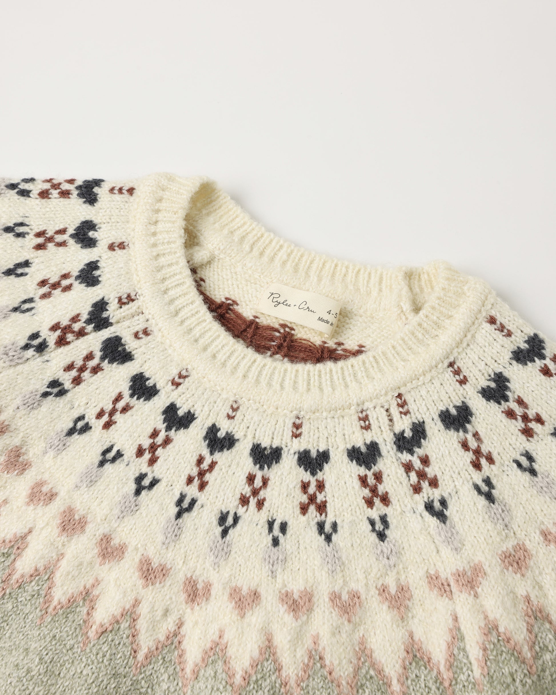 Close-up of a cream knit sweater with a Fair Isle pattern in black, brown, and dusty pink, featuring a ribbed crew neck.