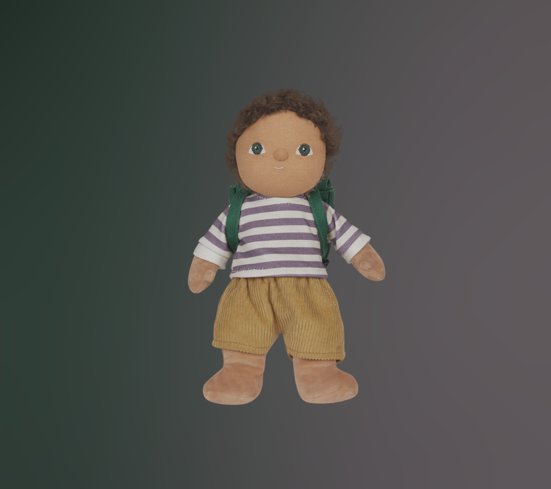 Toy doll figure of a child with green eyes and brown hair, wearing a striped purple and white shirt, brown corduroy shorts and green backpack on a dark background