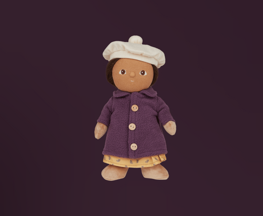 Toy doll with brown hair and brown yees wearing a purple coat, yellow patterned dress and white beret style hat on a dark background