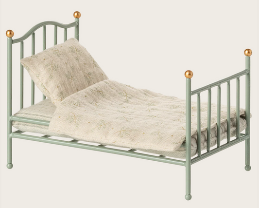 Green metal dollhouse bed with white bedding and gold accents on a white background