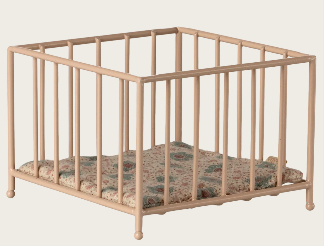 Beige metal dollhouse crib with floral mattress on a beige background