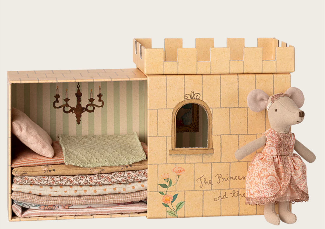 Cardboard toy castle, with blankets inside, with a mouse doll in a pink dress and crown next to it