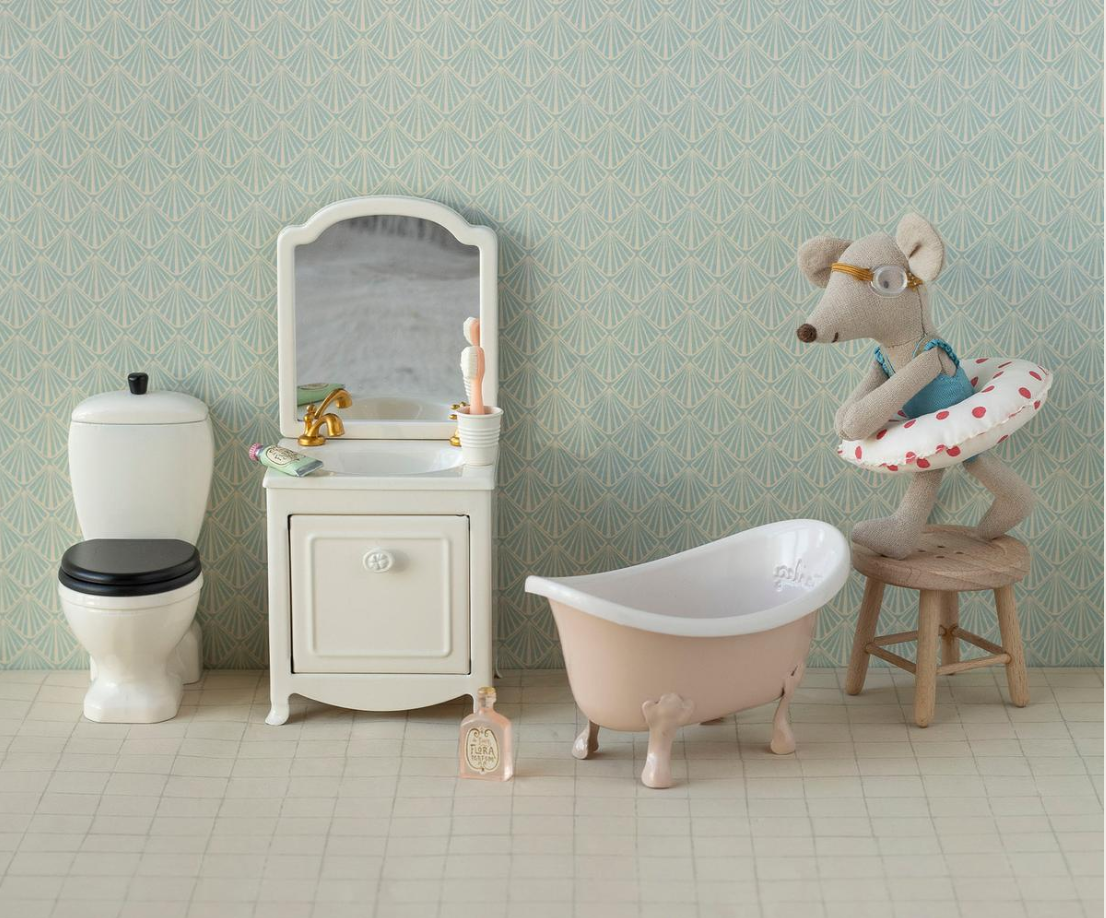 Miniature bathroom set with a bathtub, toilet, and vanity against a patterned wall.