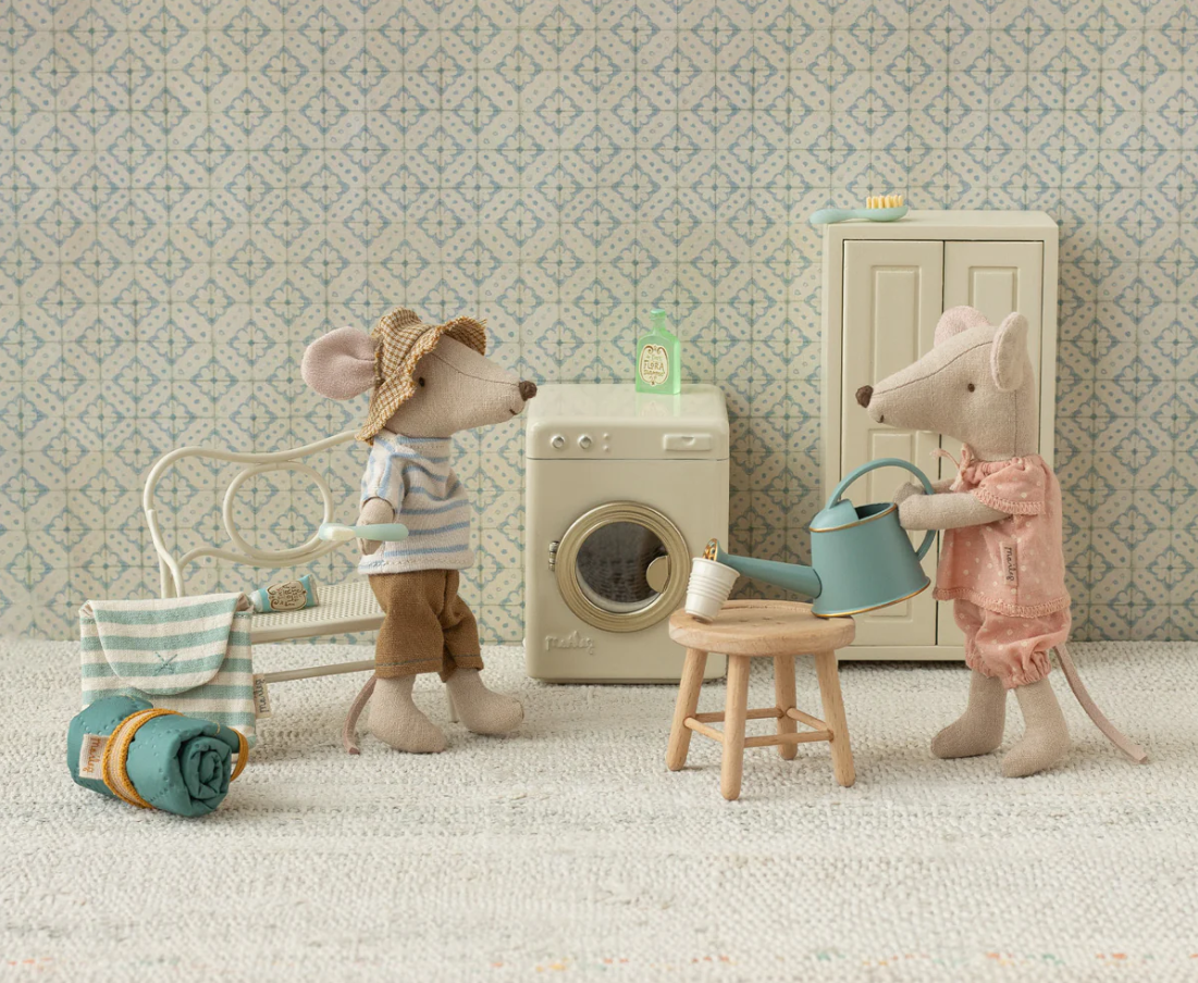 Two toy mice in a laundry room setting with a washing machine and other laundry items.