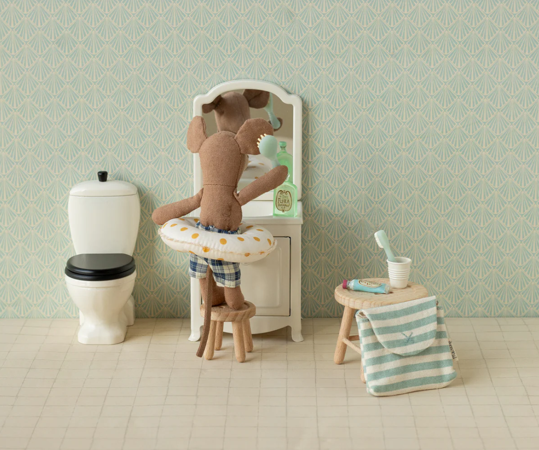 Maileg mouse doll looking in bathroom vanity mirror with doll toilet, stool, and toiletry set