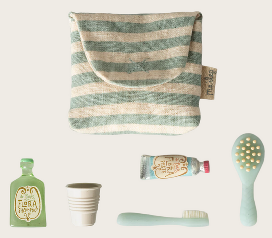 Collection of doll toiletries including a blue striped towel, shampoo bottle, cup, tube, and brush on a white background.
