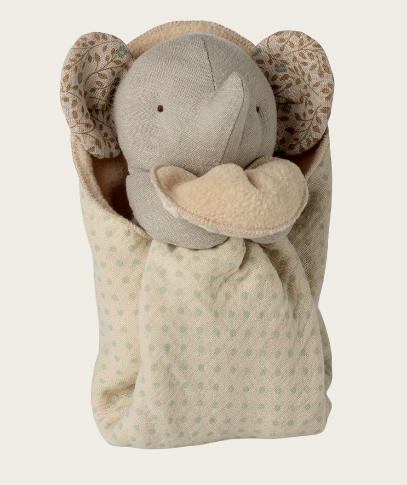 Stuffed elephant toy with floral ears wrapped in a patterned blanket on a light background