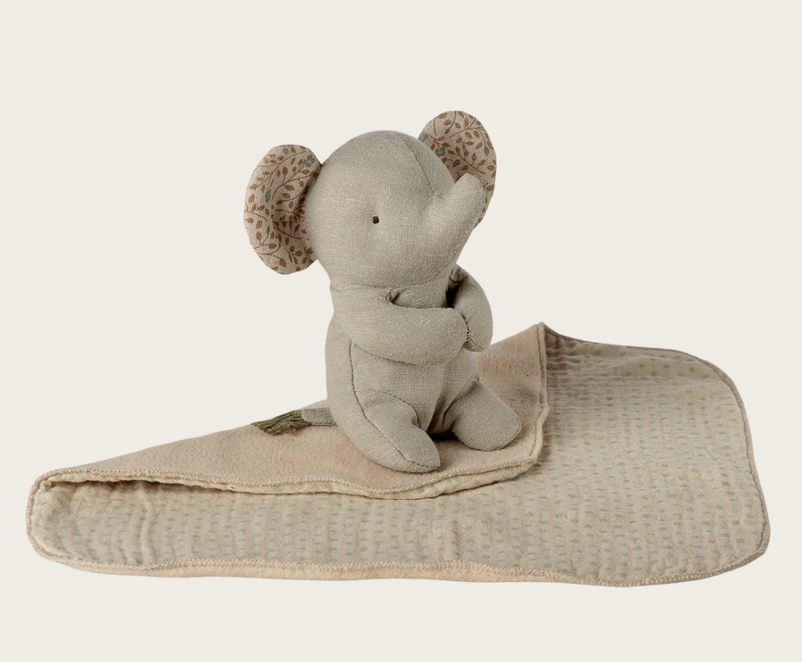 Stuffed elephant toy with floral print ears on a beige blanket against a white background