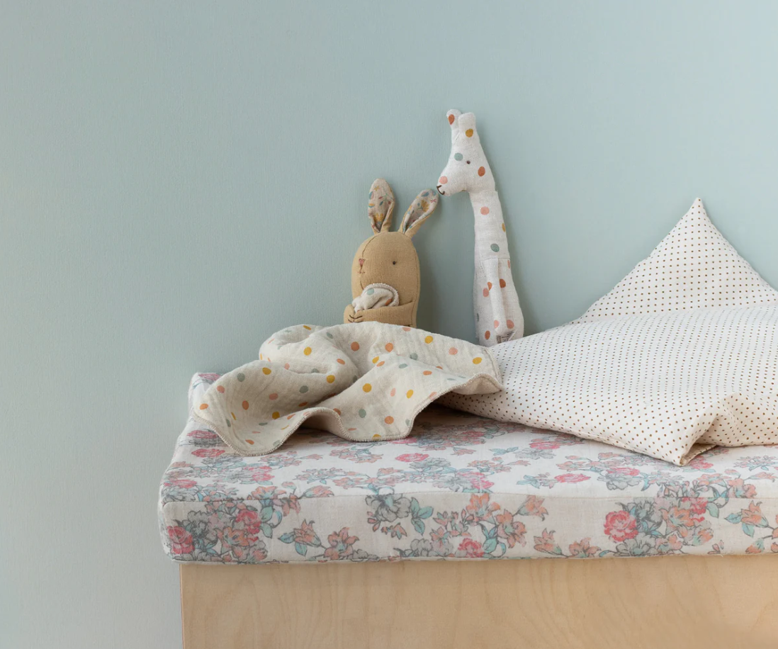 Plush bunny doll with polka dot blanket on a fabric covered cushion