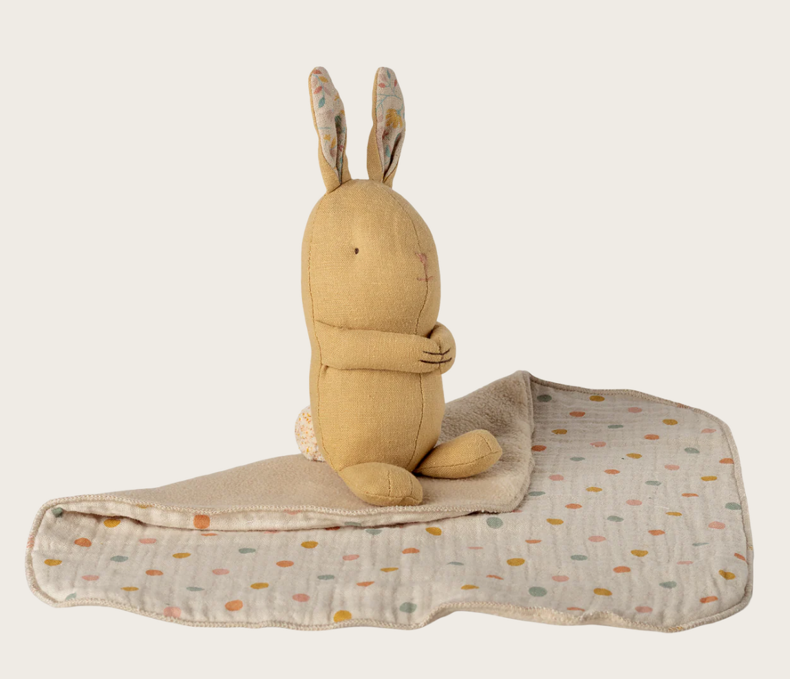 Plush rabbit toy with a blanket on a beige background