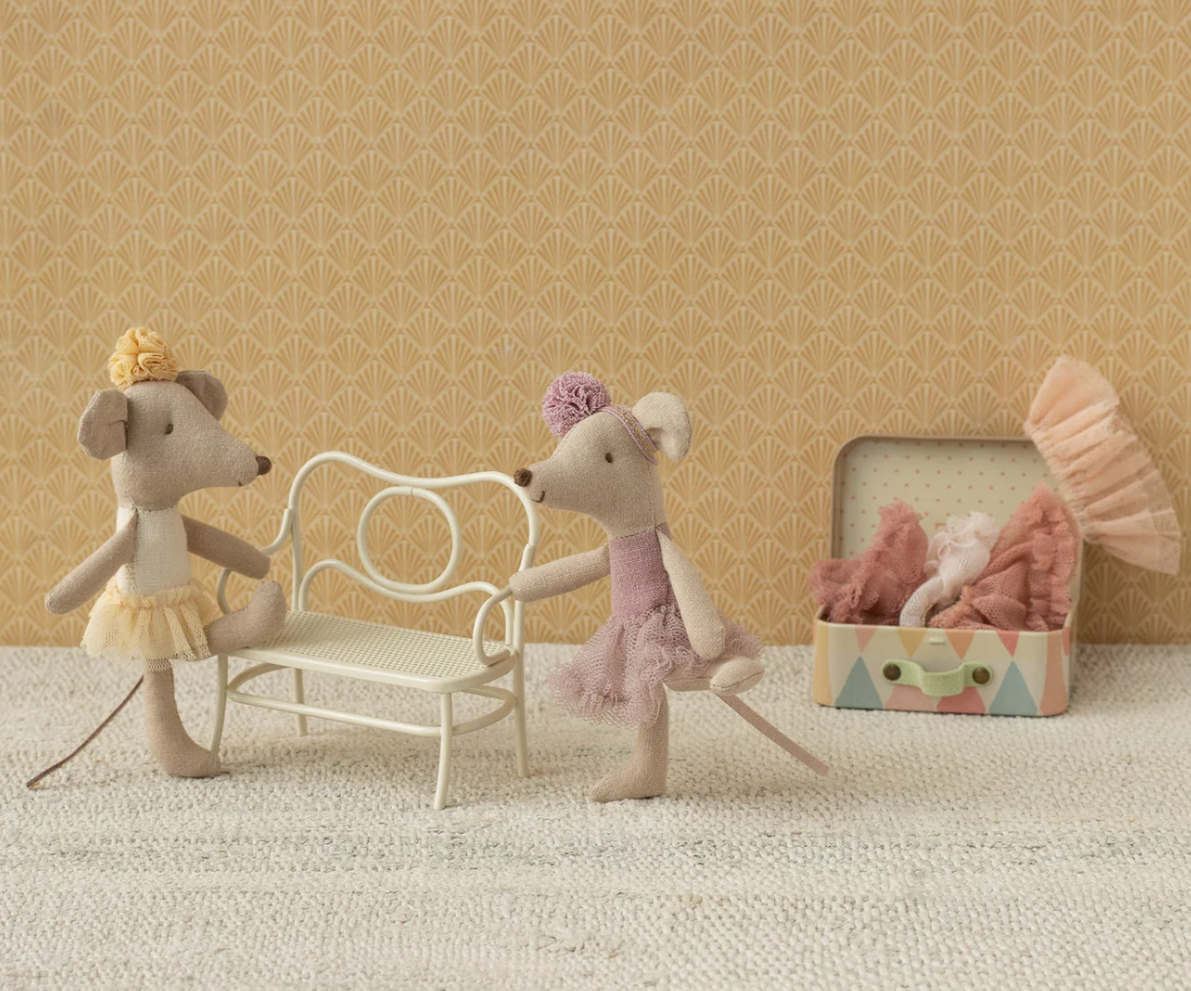 Two toy mice in a dance pose with a chair and box on a textured surface and patterned wall background.