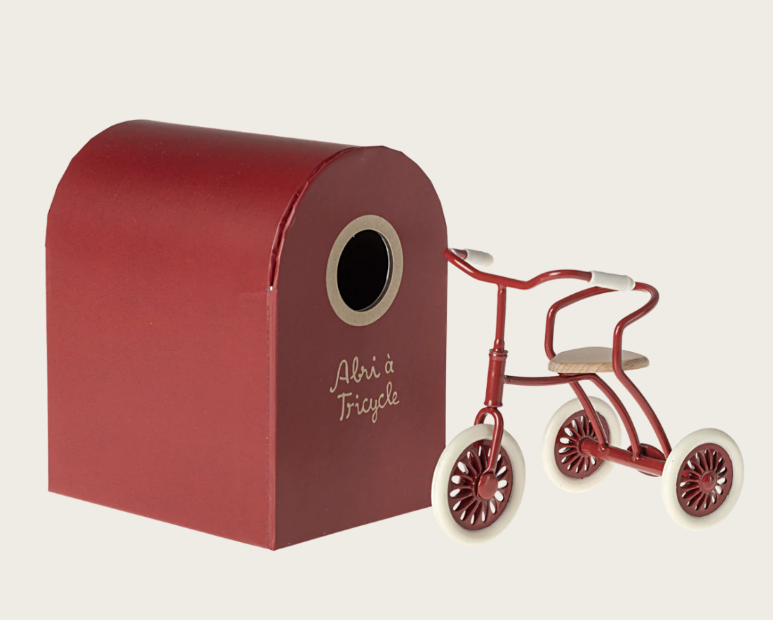 Small red toy dollhouse-sized tricycle with red garage box on a white background