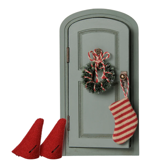 Sage green Maileg Christmas dollhouse door with wreath, stocking, and red hats, all on a white background