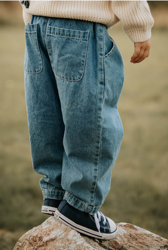 Child standing on a rock wearing denim pants and black converse shoes