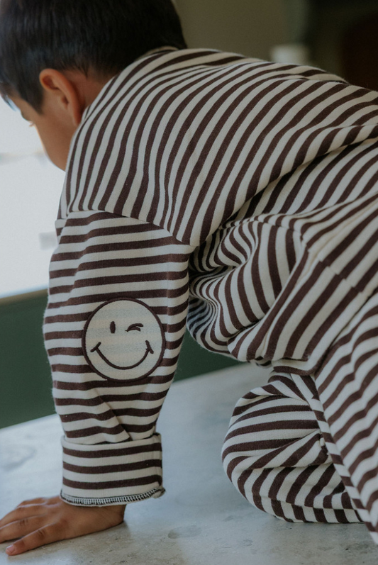 Child wearing brown and ivory striped sweatshirt with smiley face patches on the elbows