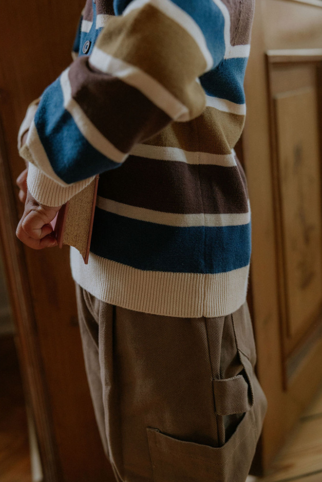 Close up photo of child wearing the duna cargo pants and a striped sweater holding an antique book