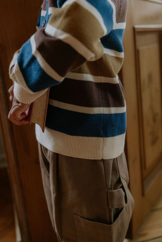 Close up photo of child wearing the duna cargo pants and a striped sweater holding an antique book