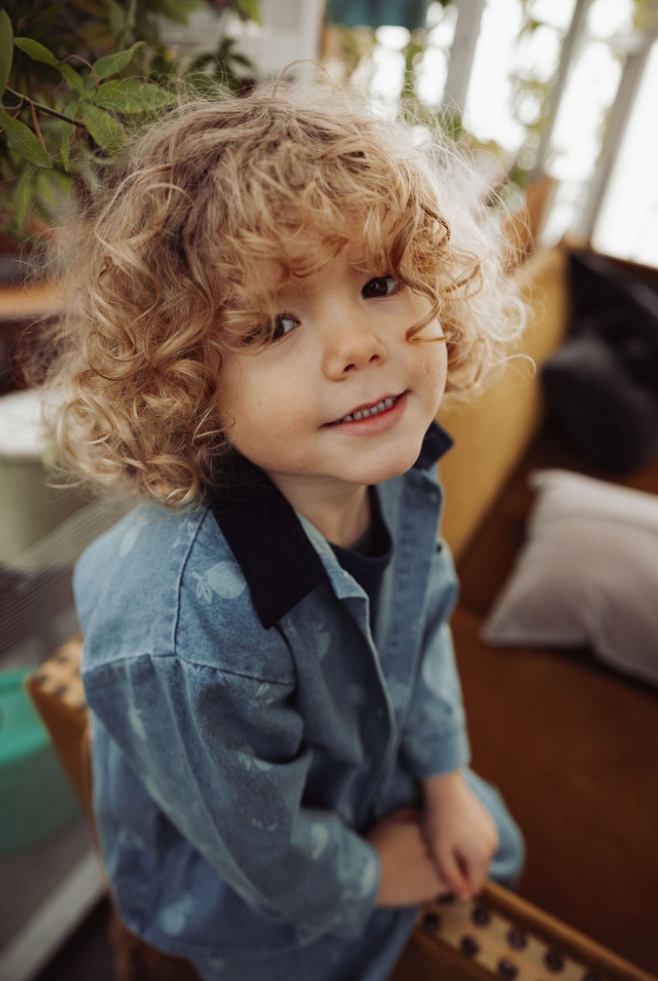 Child wearing denim shirt in a blurred background in a living room setting
