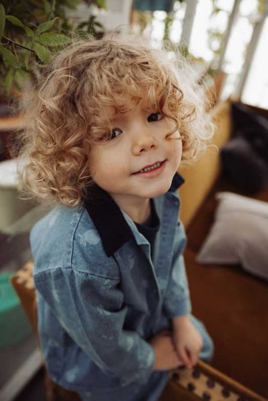 Child wearing denim shirt in a blurred background in a living room setting