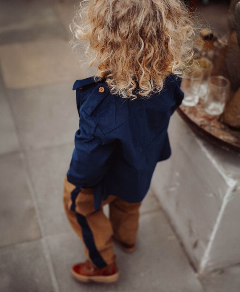 Child wearing Blue collared button down children's top and brown pants in an exterior street setting