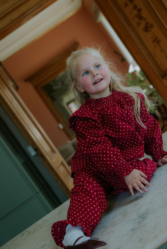 Child wearing red ruffly long sleeve blouse with white polka dots sitting in an interior kitchen setting