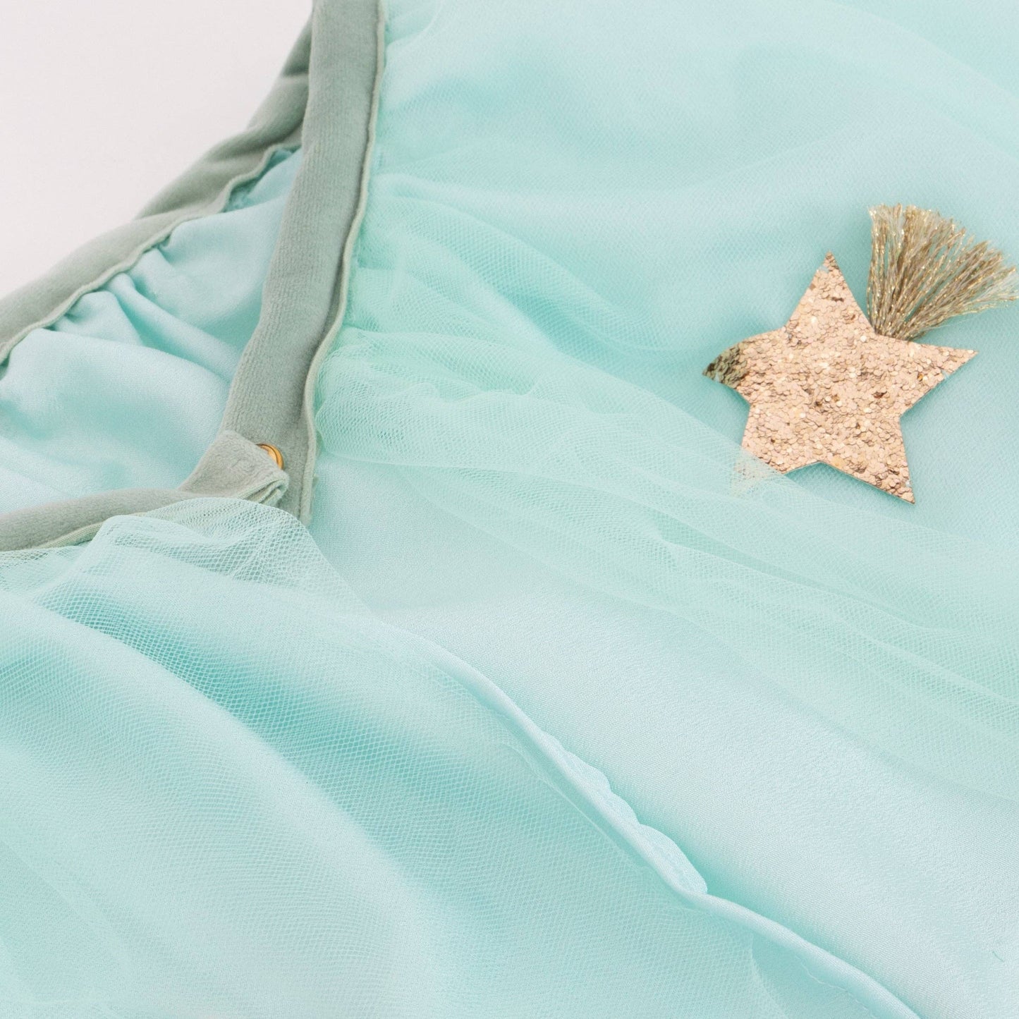 Close-up of a light green tulle fabric with a gold star and tassel detail.