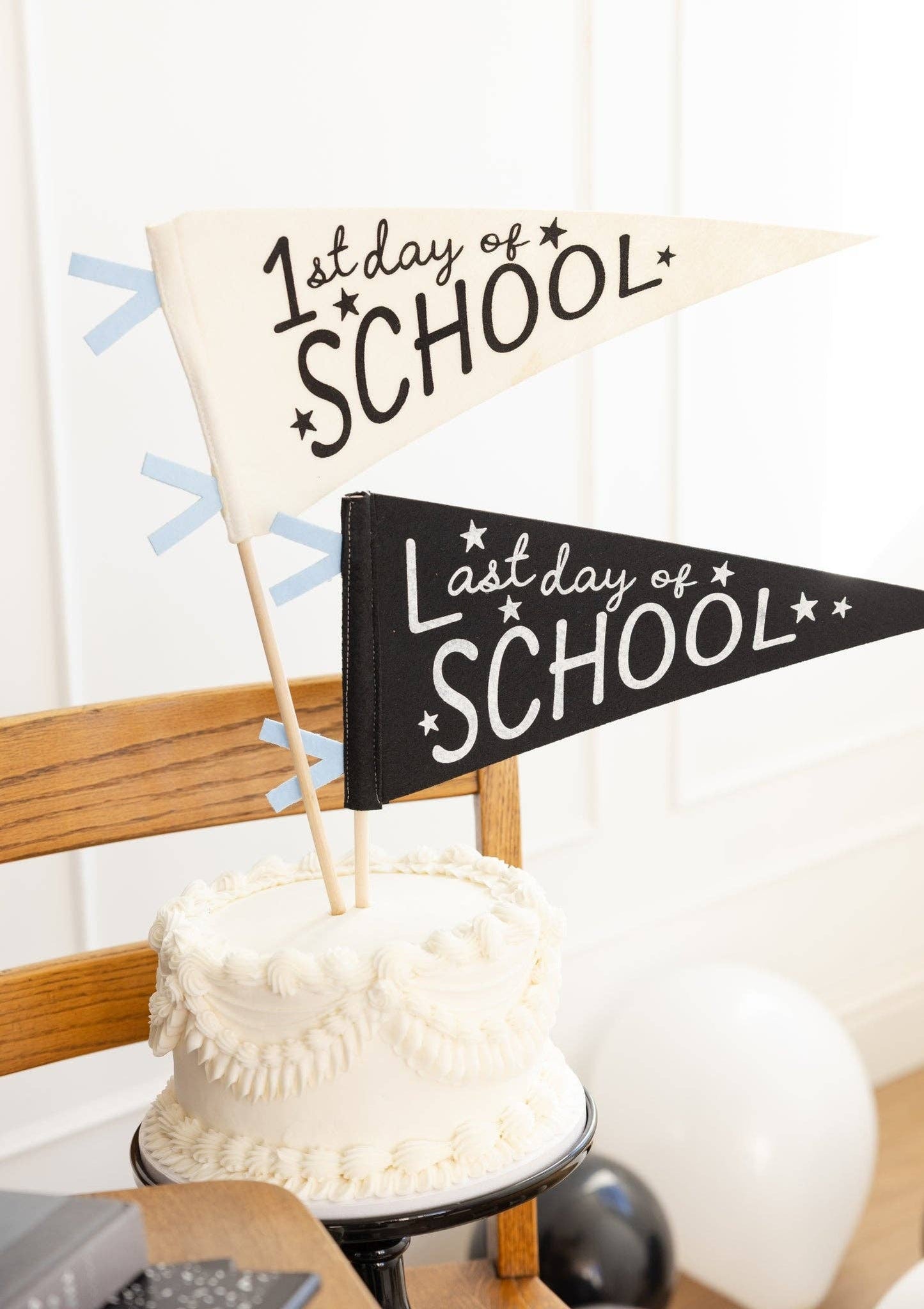 Two pennants on a in a white cake, one black one that says "last day of school" and one white one that says "first day of school"