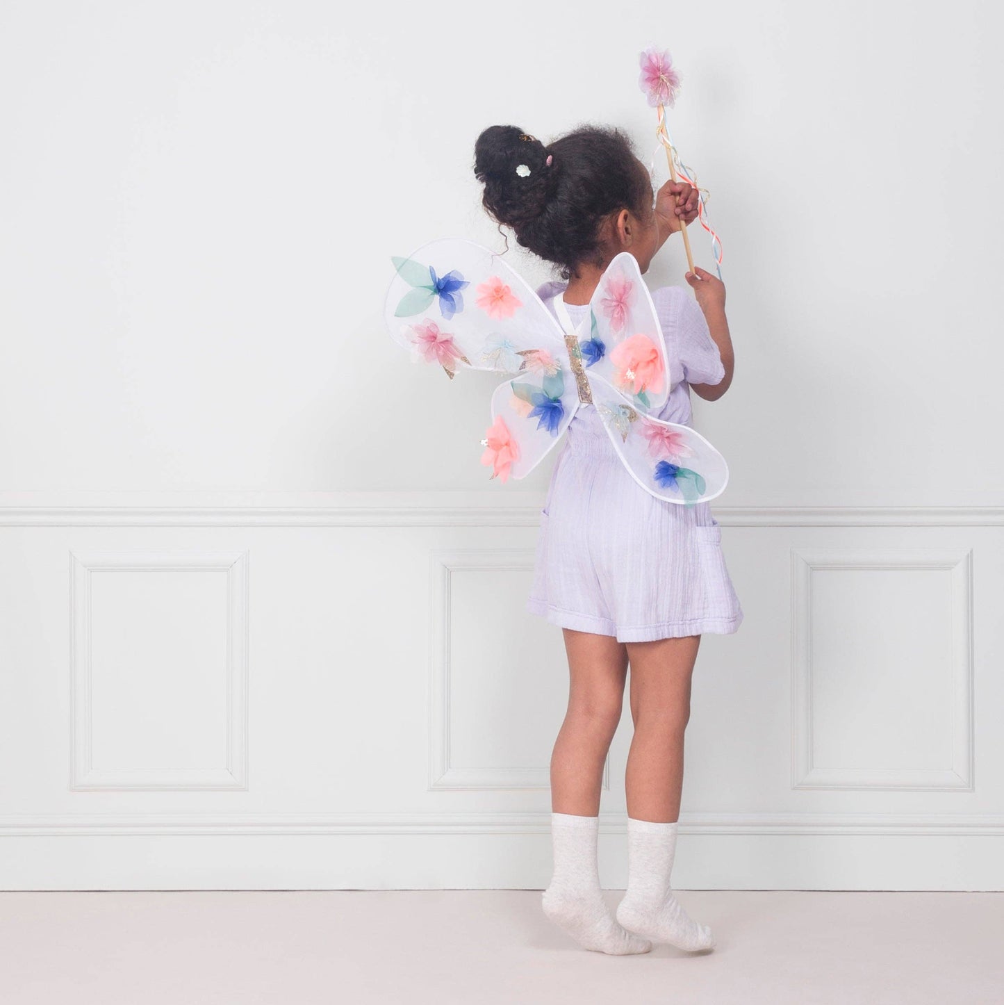 Child wearing fairy wings and holding a wand against a white wall