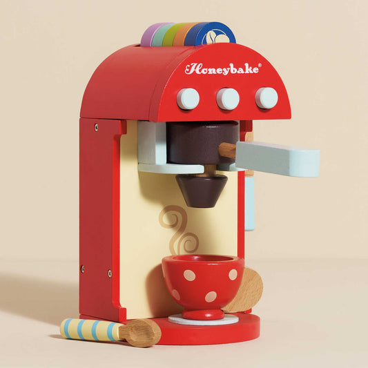 Red toy coffee machine with polka dot cup and colorful accents on a beige background