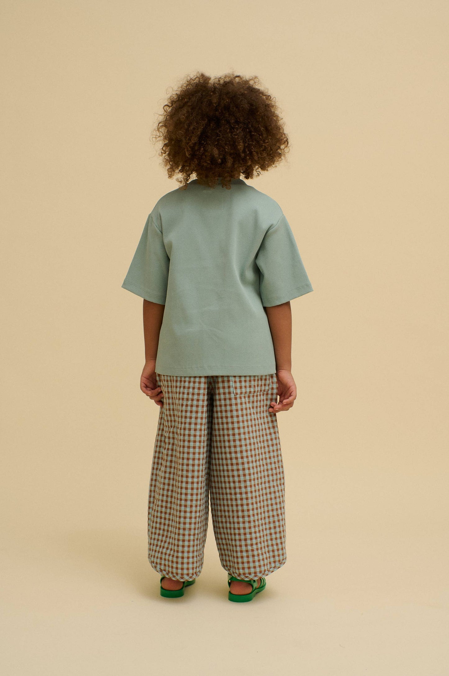 Child wearing a light green shirt and checkered pants on a beige background