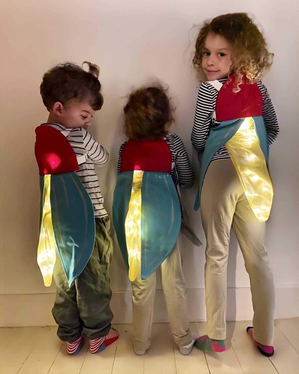 Three children in colorful costumes with light-up elements standing against a plain background.