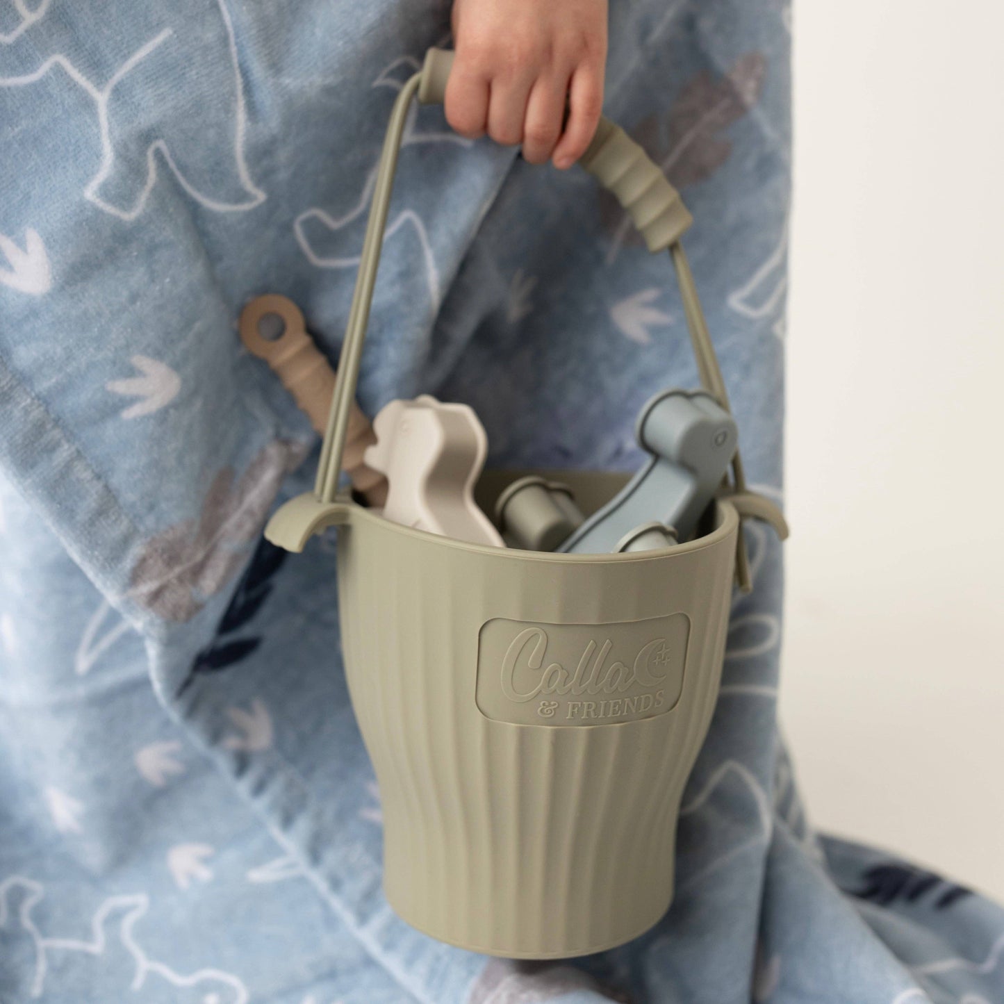 Green sand pail with tools held by a child on a blue blanket