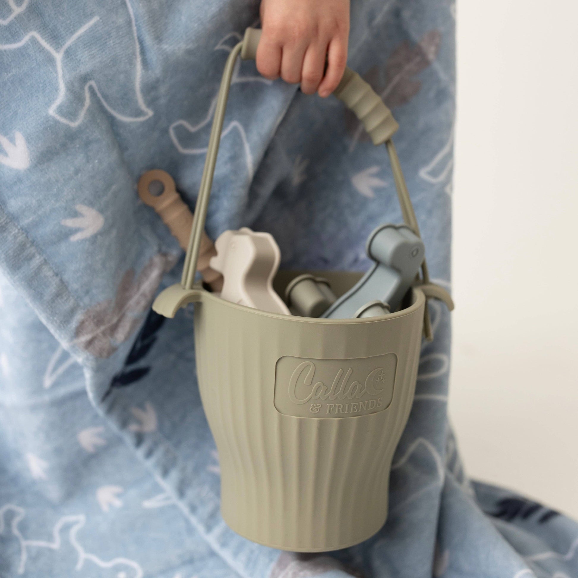 Green sand pail with tools held by a child on a blue blanket