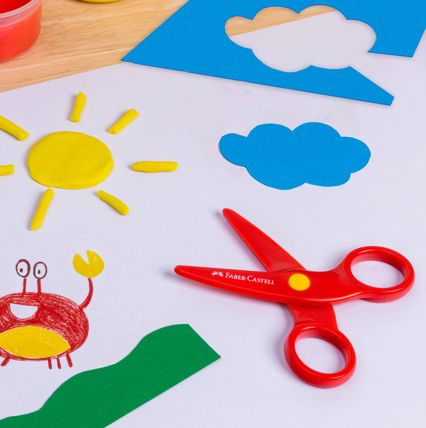 Colorful paper cutouts of a sun, cloud, and crab with red scissors on a white surface.