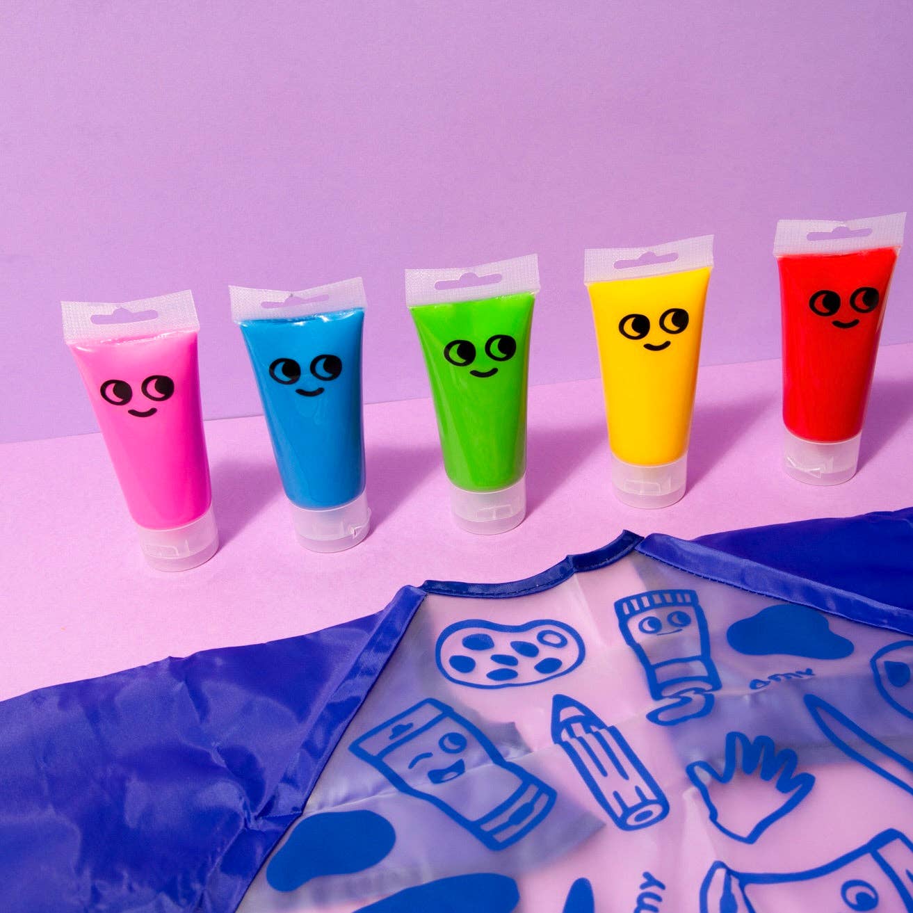 Five tubes of colorful paint with smiley faces on a purple background, with a blue art smock below.