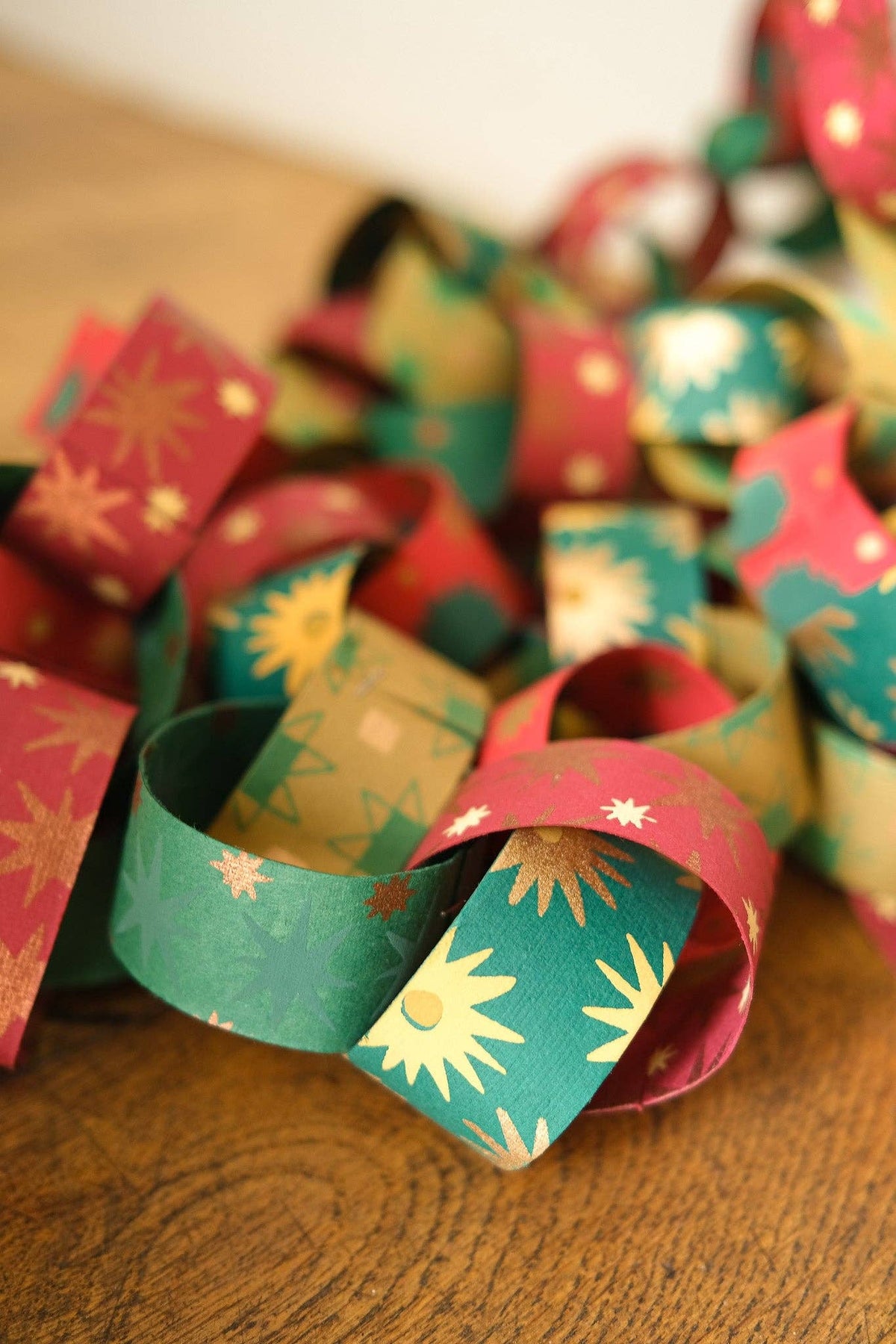 Red, green and gold patterned paper chain links resting on a wooden table.