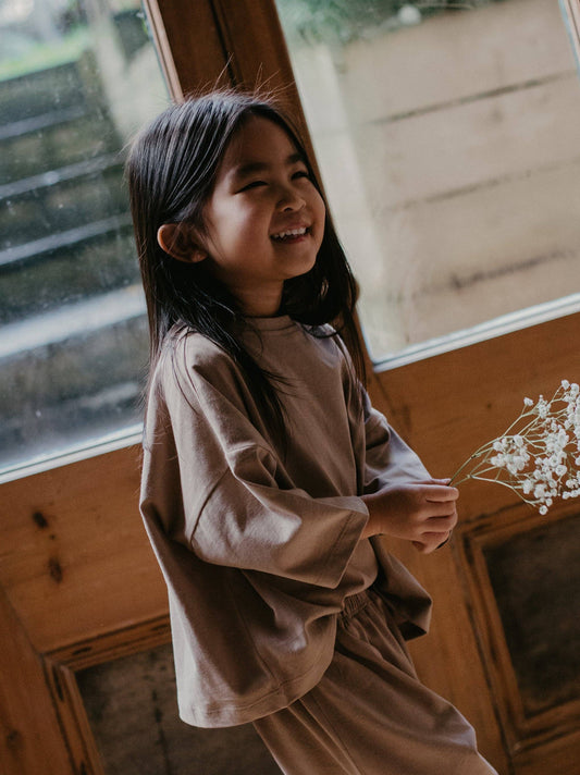 Young girl in a brown oversized t-shirt holding a small bouquet indoors.