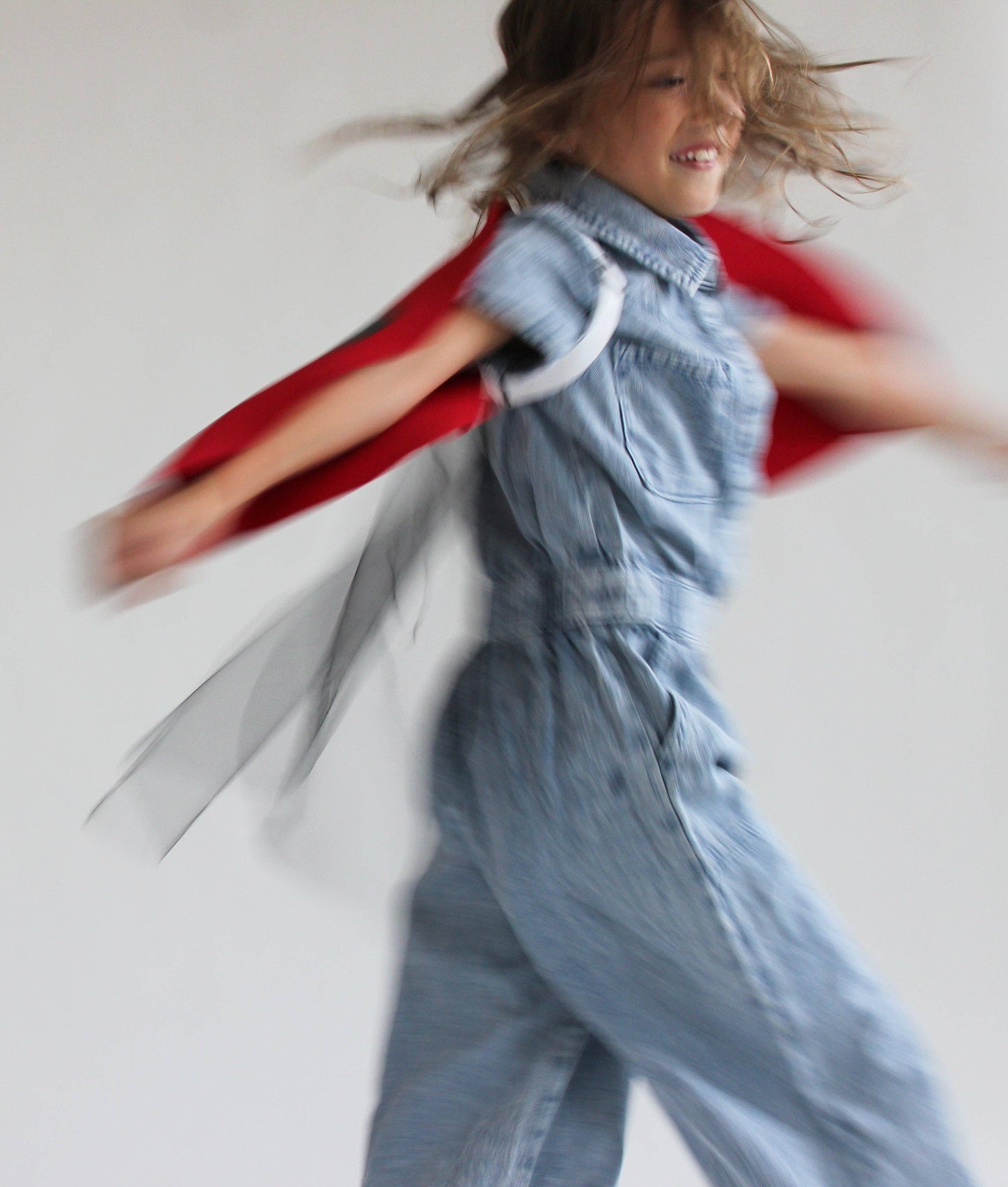 Child in a denim outfit with a red cape running on a white background